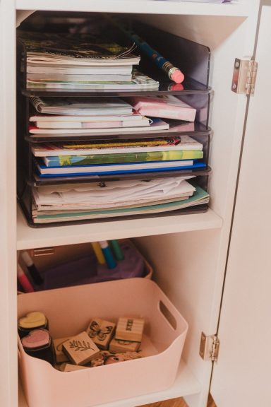 Étagère avec des classeurs, livres et un panier rose contenant des tampons.